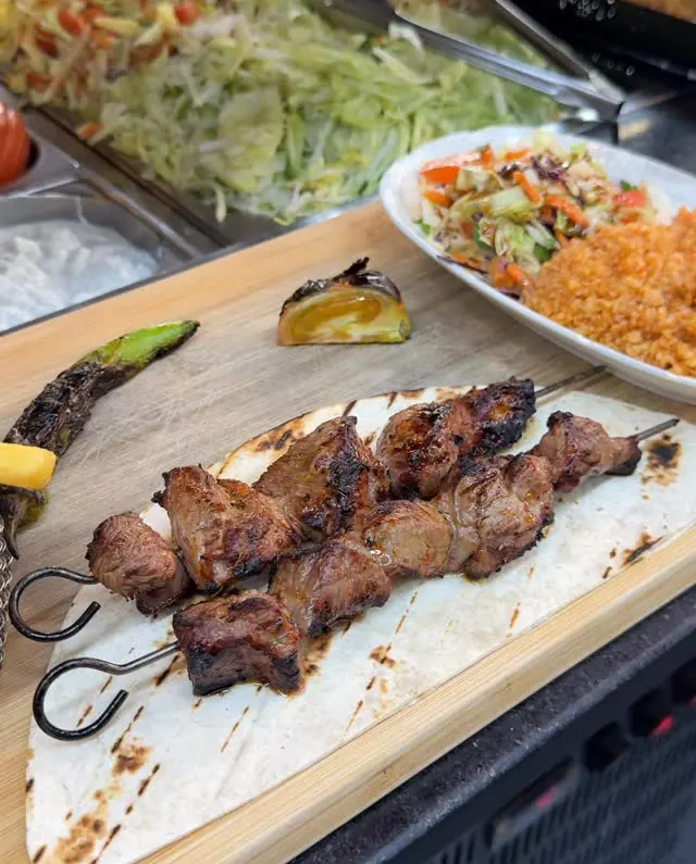 Brochettes d'agneau grillées, servies sur galette avec blé et salade
